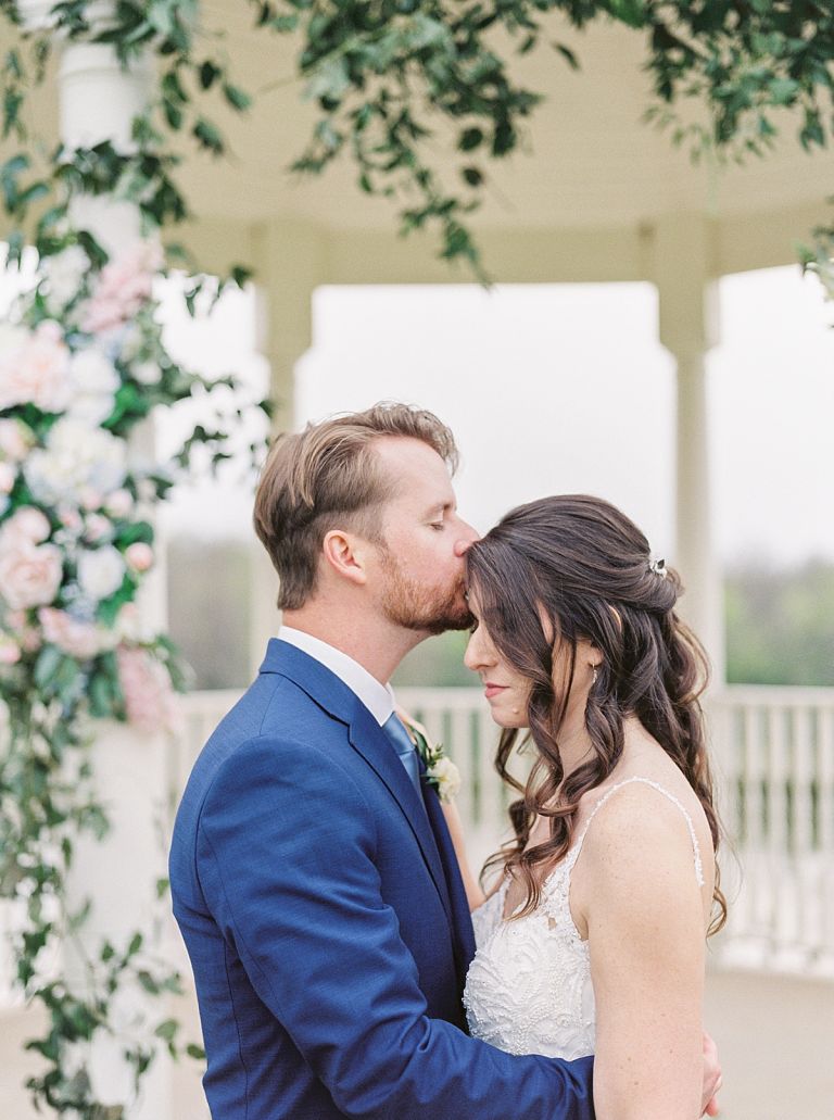 Bride and groom kiss under gazebo covered in flowers, Milestone Mansion wedding, southern wedding, pink and white wedding flowers