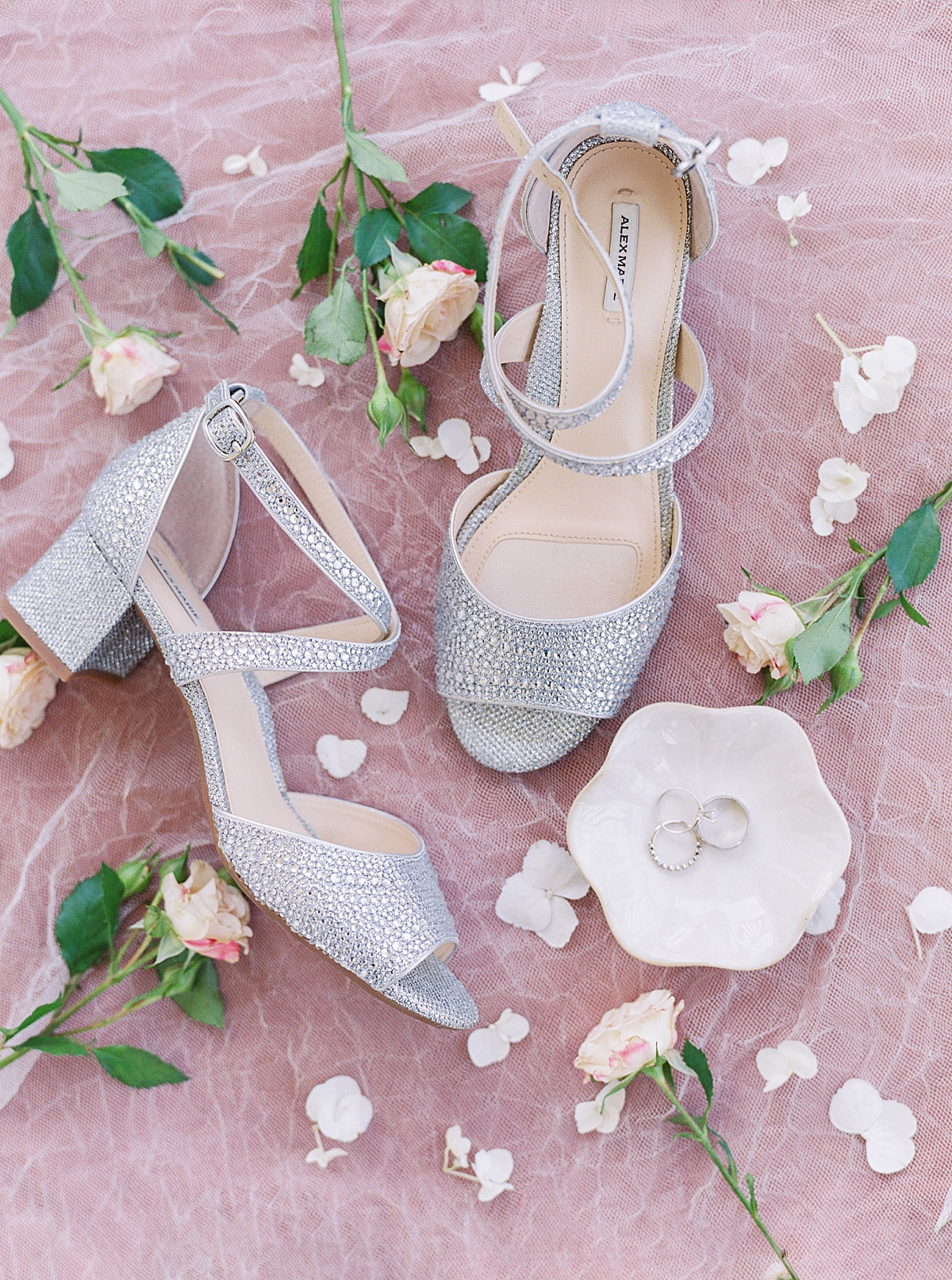 Bride's sparkly silver shoes on pink background with rings in scalloped marble ring dish