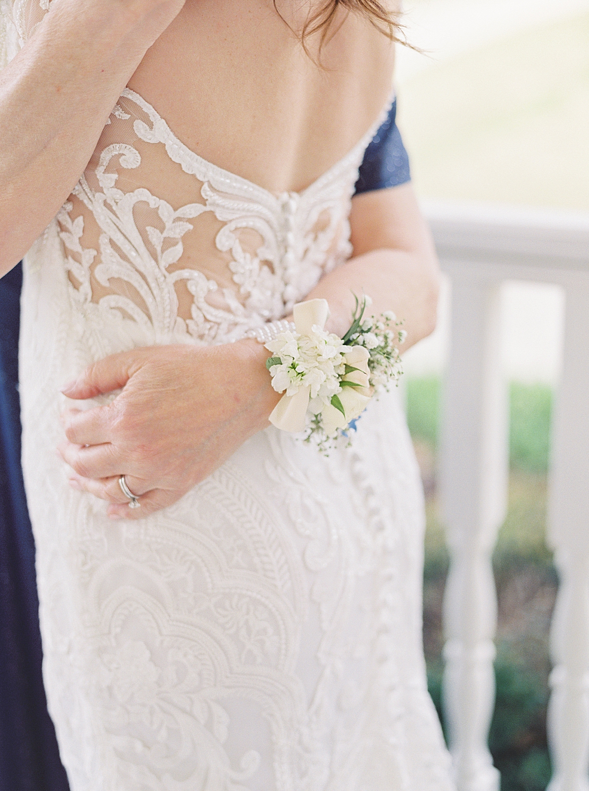 Mother-of-the-bride wrist corsage, white wedding flowers, bride in lace white dress with low sheer back