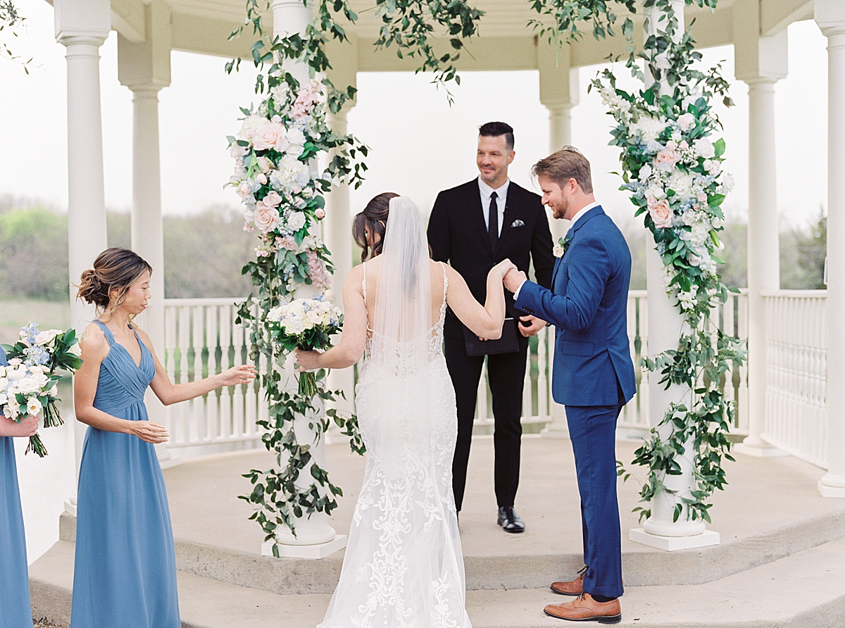 Bride and groom in wedding ceremony in front of white gazebo with flower arch