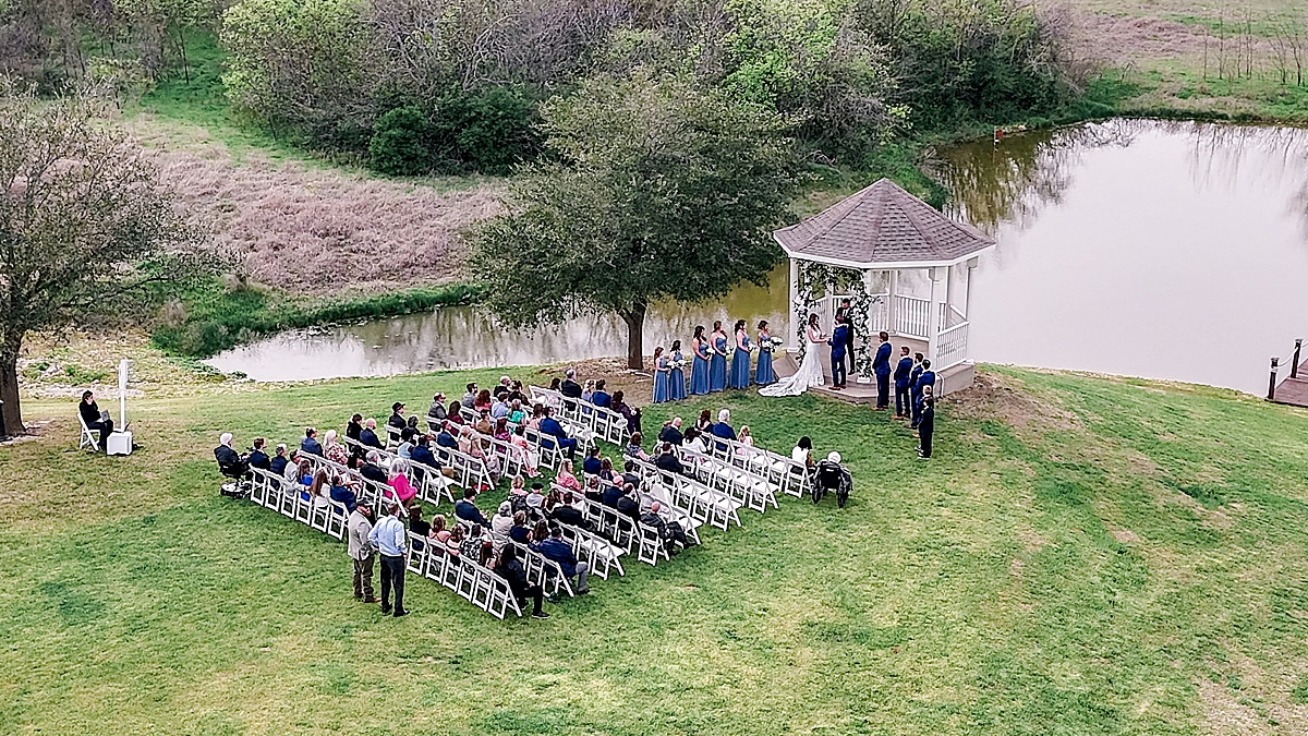 Drone photo of outdoor wedding ceremony in front of pond, mansion wedding