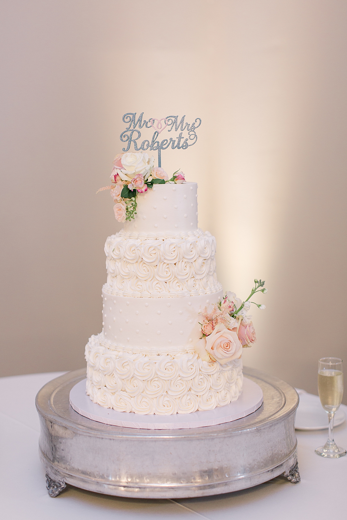 White four tier wedding cake with buttercream, silver glitter personalized cake topper with bride and groom names, fish flowers on a wedding cake